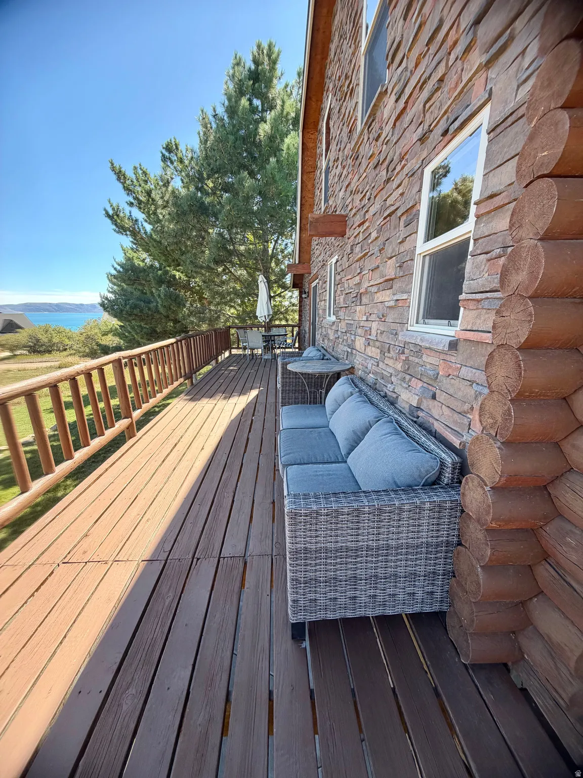 Expansive outdoor deck with natural wood railing, stone veneer siding, and a log-style corner accent