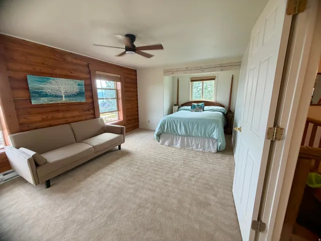 Carpeted room featuring a ceiling fan, a wood-paneled accent wall, and two windows with natural light