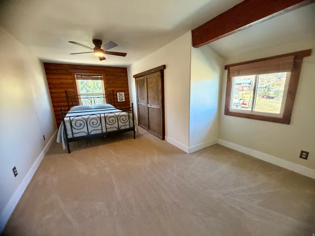 Carpeted interior with wood-paneled accent wall, exposed wood beam, and wooden window trim