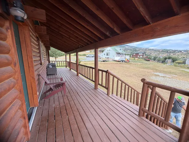 Expansive covered porch featuring a log cabin exterior, wood-finish decking, and rustic wood railings