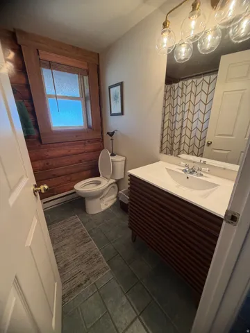 Bathroom featuring a wood-panel accent wall, square-tiled flooring, and a vanity with a white countertop and integrated sink