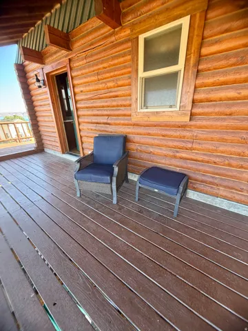 Covered exterior porch featuring log siding, composite decking, and a wall-mounted light fixture
