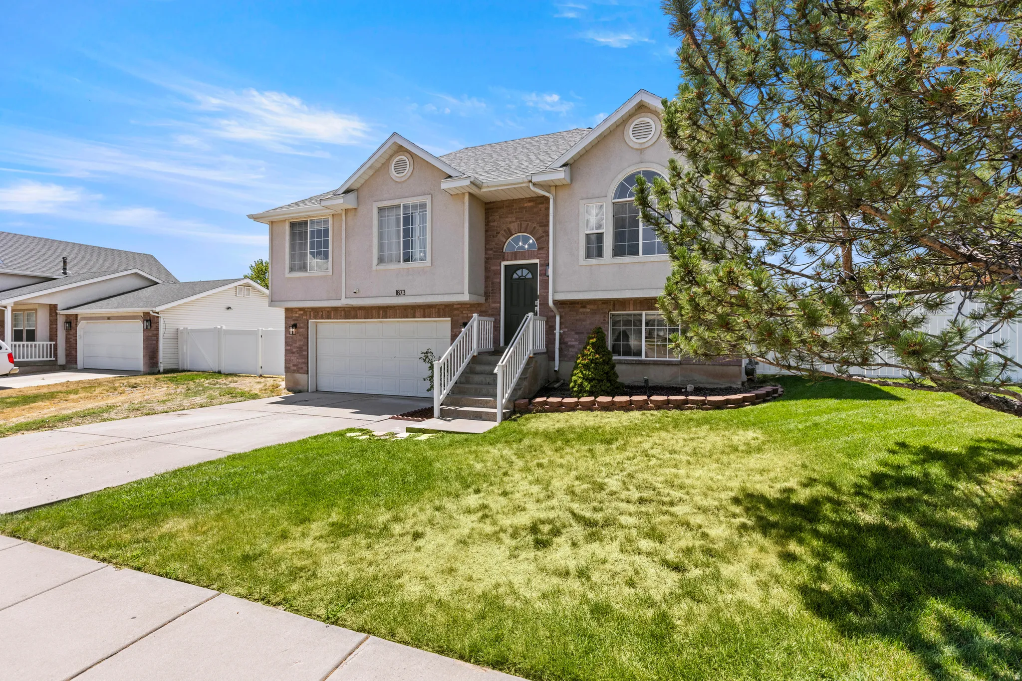 Front exterior featuring a two-car garage, brick facade, arched window, and mature landscaping