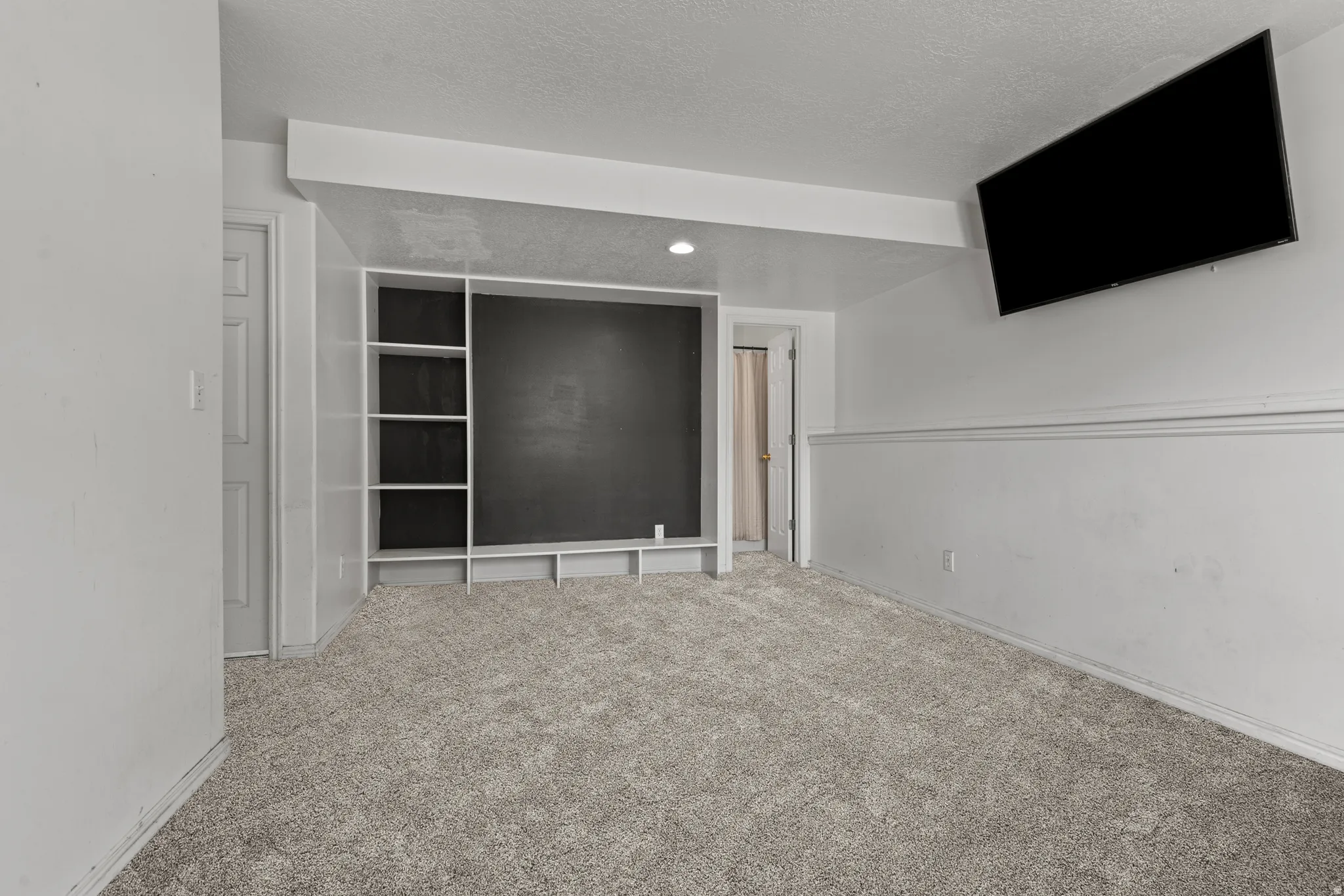 Carpeted room featuring a built-in shelving unit with a dark back panel and a mounted flat-screen display. *Carpet is photoshopped in, ment to match new carpet.
