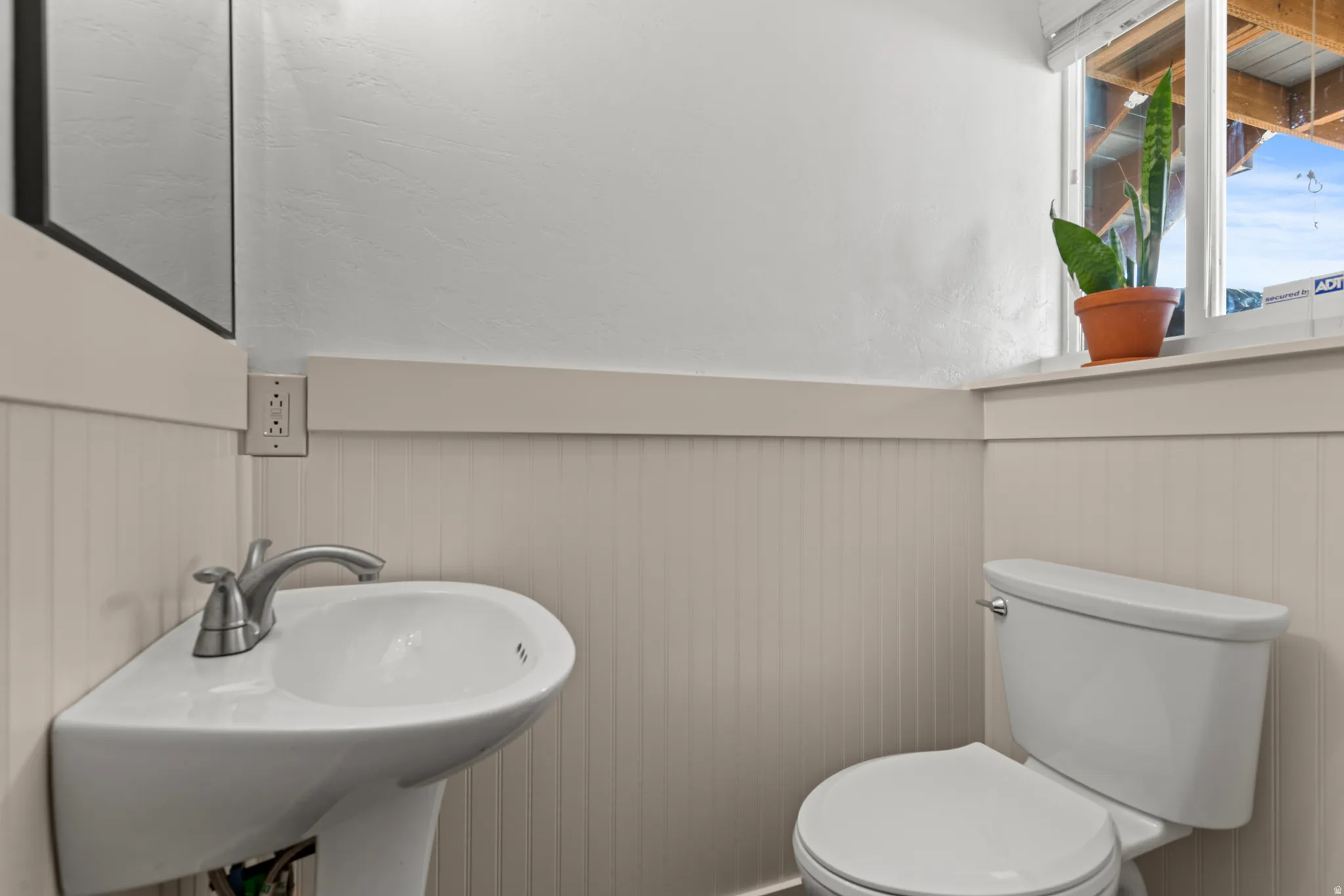 Pedestal sink with chrome faucet, toilet, and beadboard wainscoting