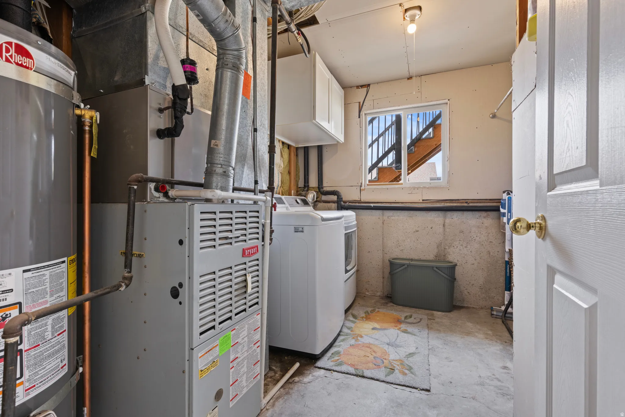 Dedicated utility area featuring a Rheem water heater, Bryant furnace, washer, dryer, and a storage cabinet