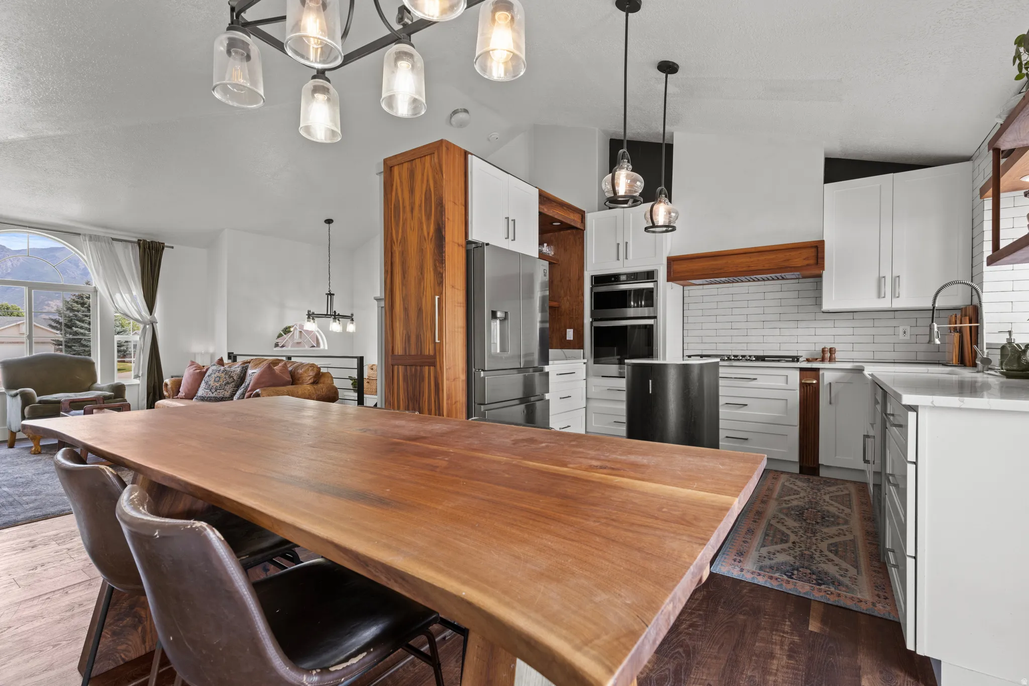 Spacious kitchen and dining area featuring a live-edge wood dining table, white shaker cabinetry, stainless steel appliances, and a subway tile backsplash