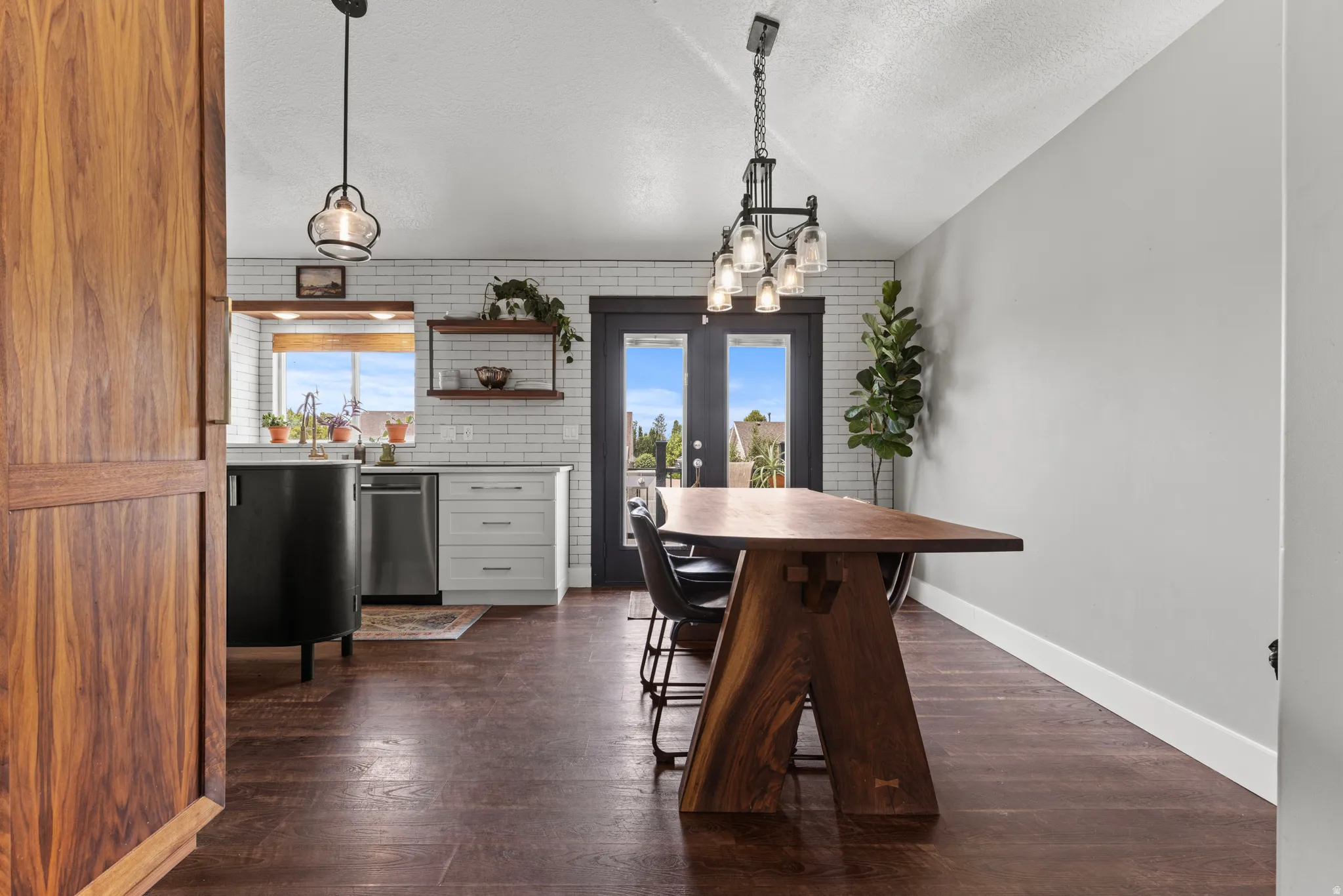 Open-concept kitchen and dining area featuring wood-finish flooring, white subway tile backsplash, light gray cabinetry, and dark French doors leading outdoors