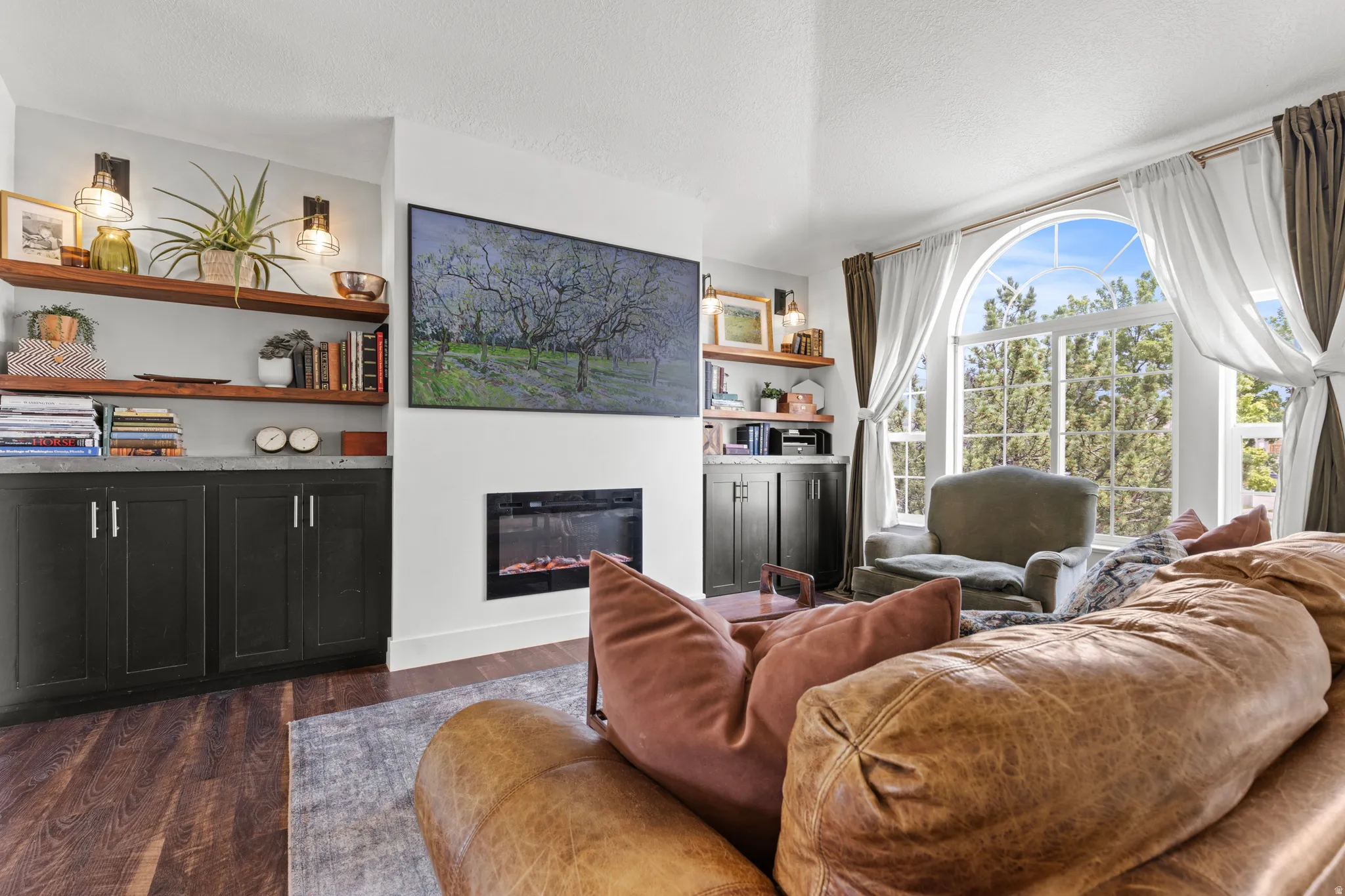 Spacious living area featuring wood-finish flooring, an arched window, and a built-in electric fireplace