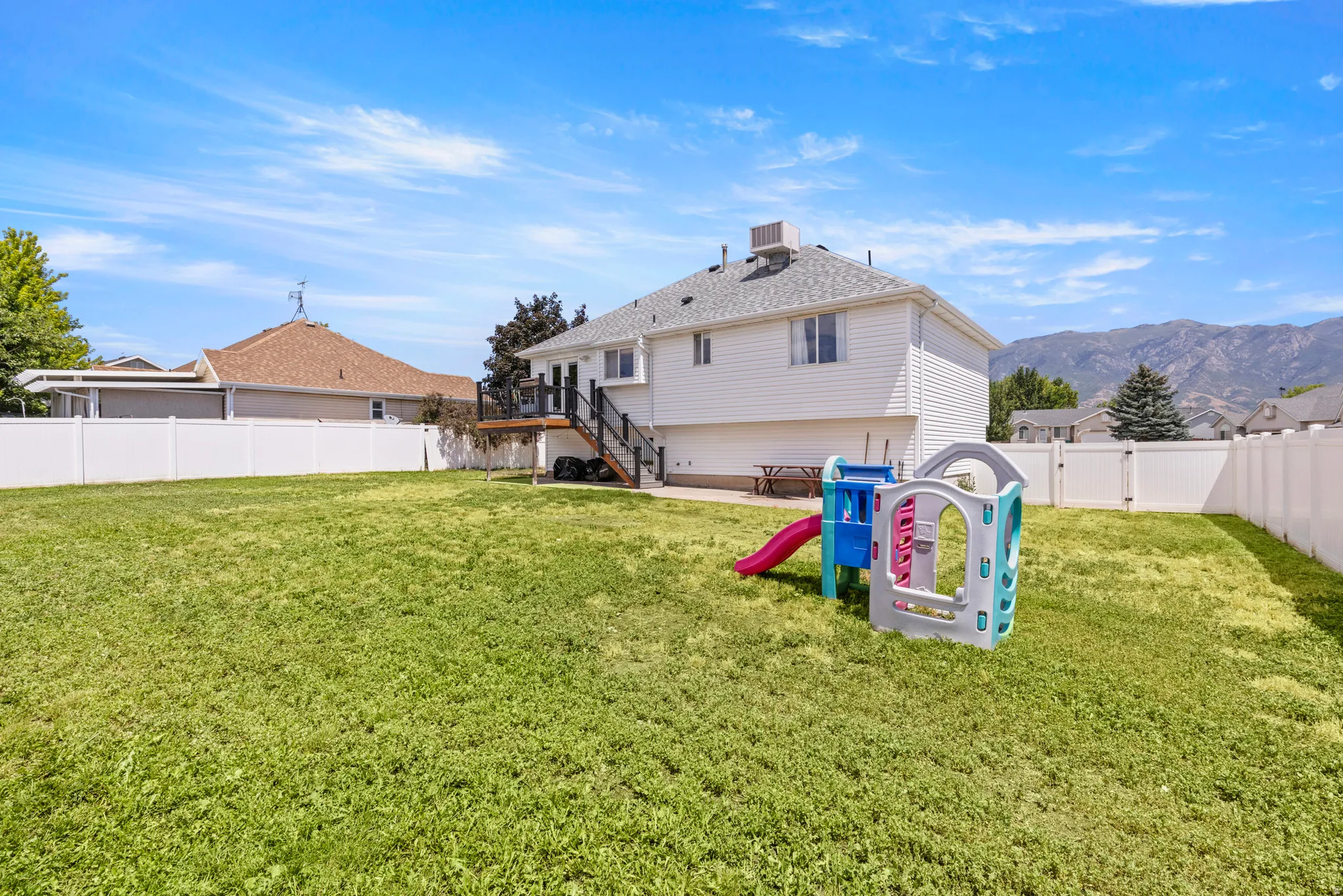 Spacious backyard featuring a manicured lawn, white vinyl fencing, and a multi-level deck with stairs