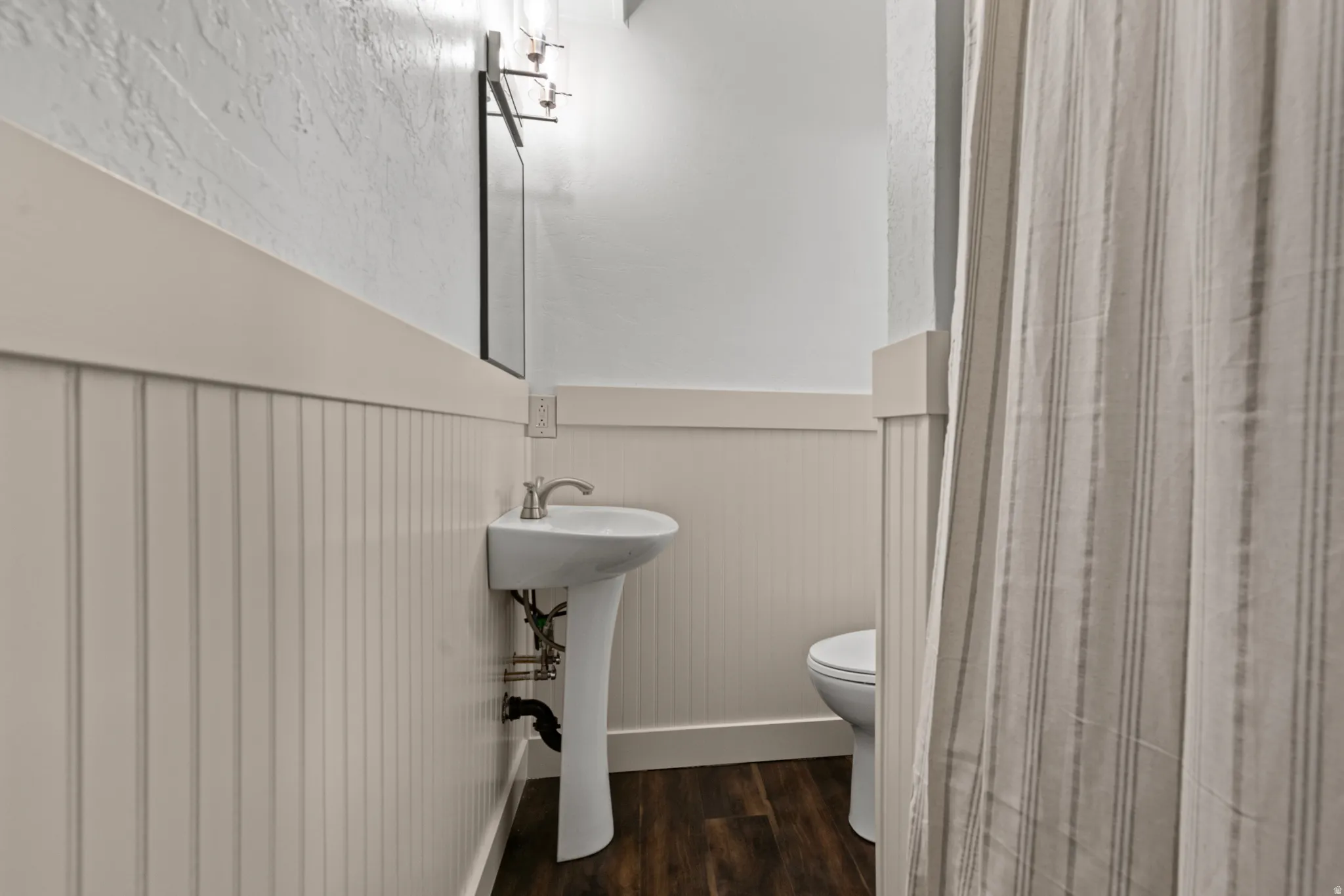 Pedestal sink with brushed nickel faucet, beadboard wainscoting, and wood-finish flooring