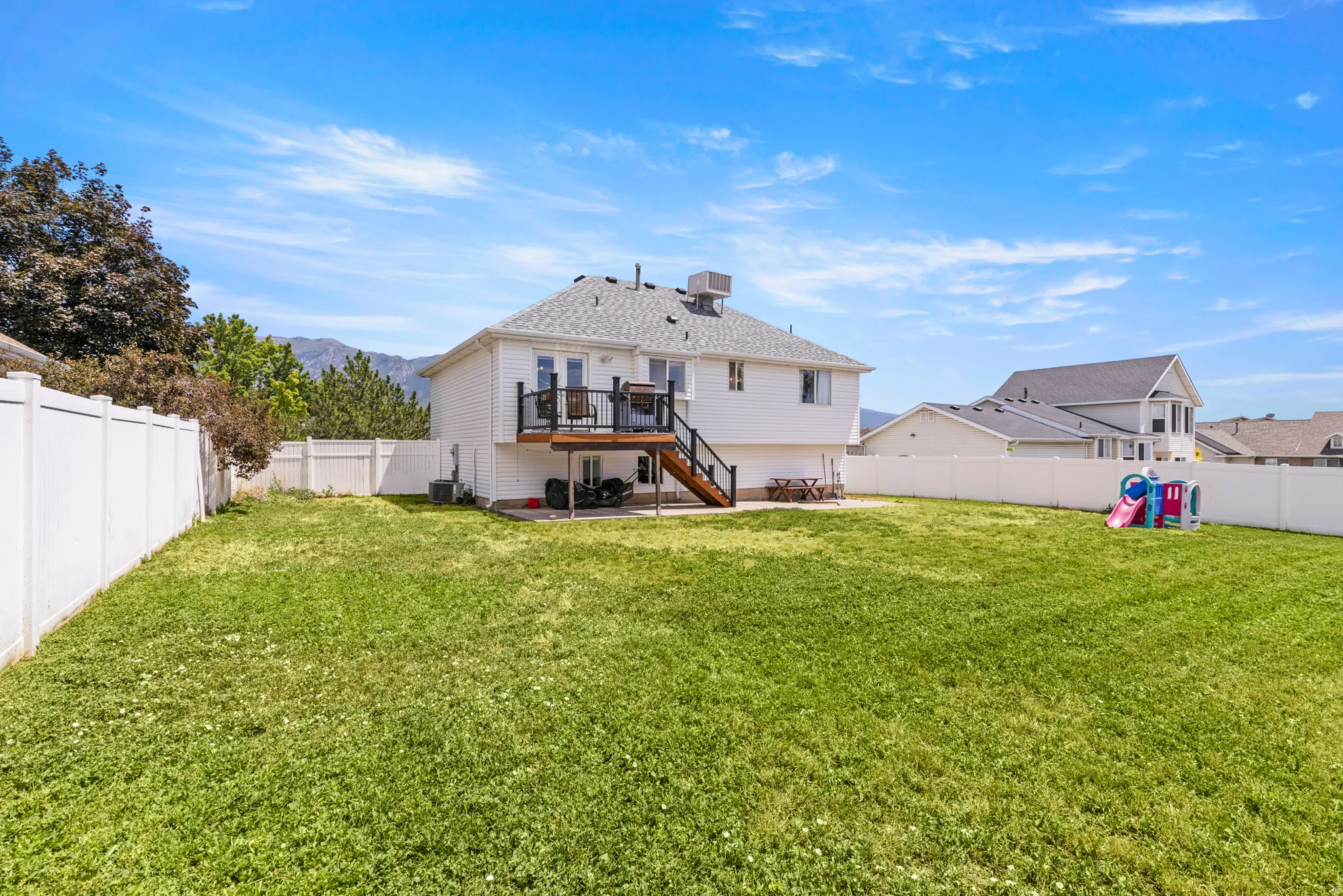 Expansive grassy backyard featuring a white vinyl privacy fence, a multi-level deck with dark railing, and a walk-out lower level