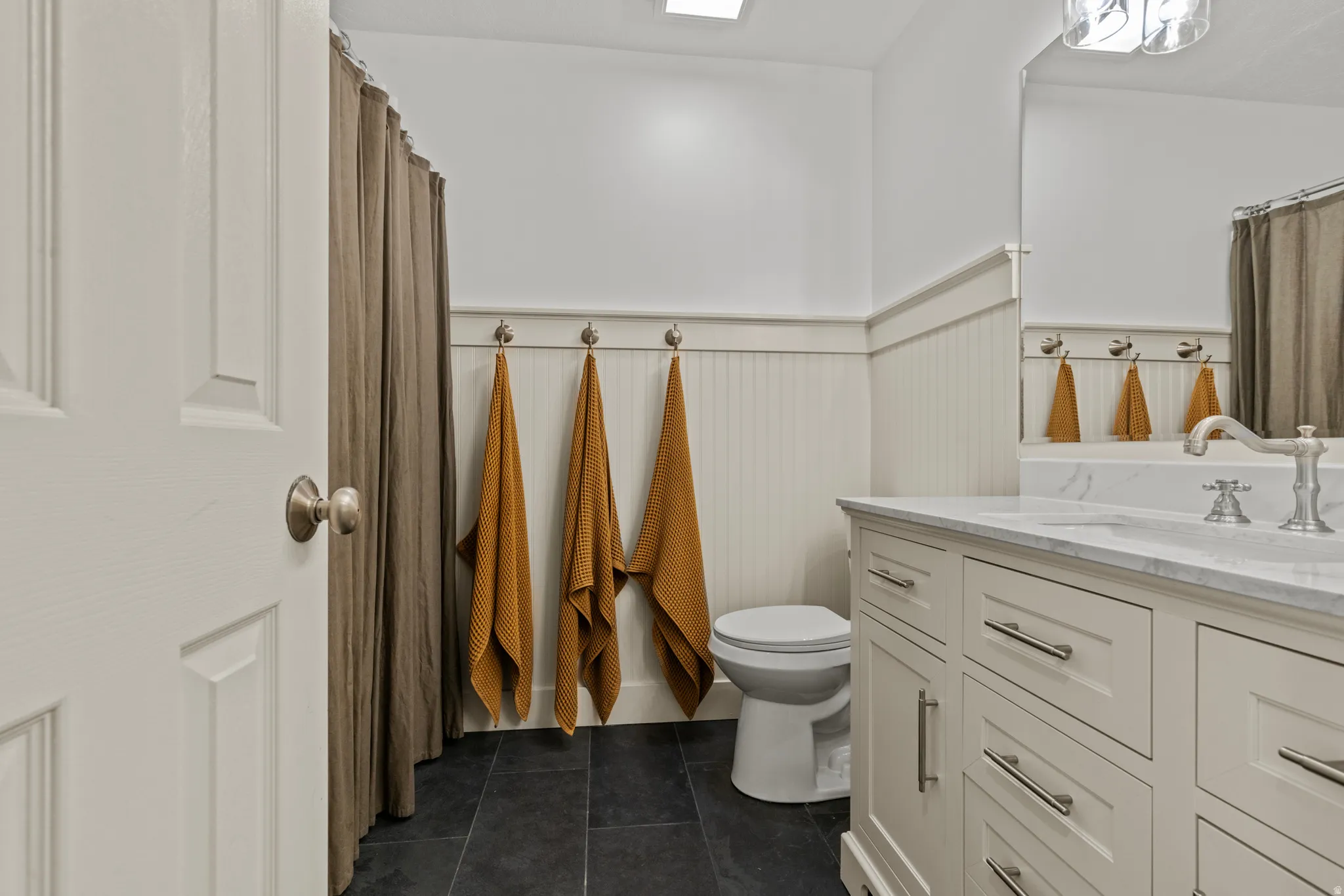 Bathroom featuring a single vanity with a marble-look countertop, white cabinetry with brushed nickel hardware, and dark tile flooring