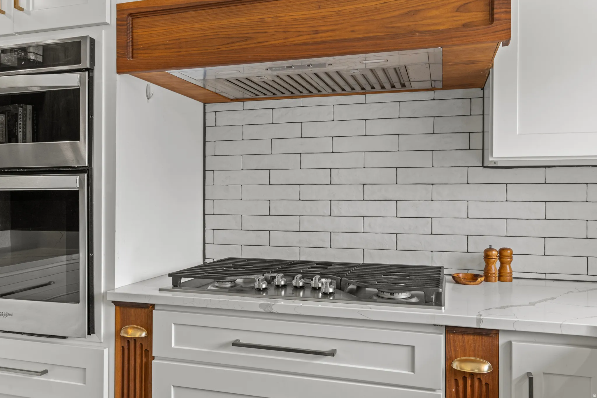 Modern kitchen featuring a stainless steel gas cooktop, white subway tile backsplash, and a rich wood-tone range hood
