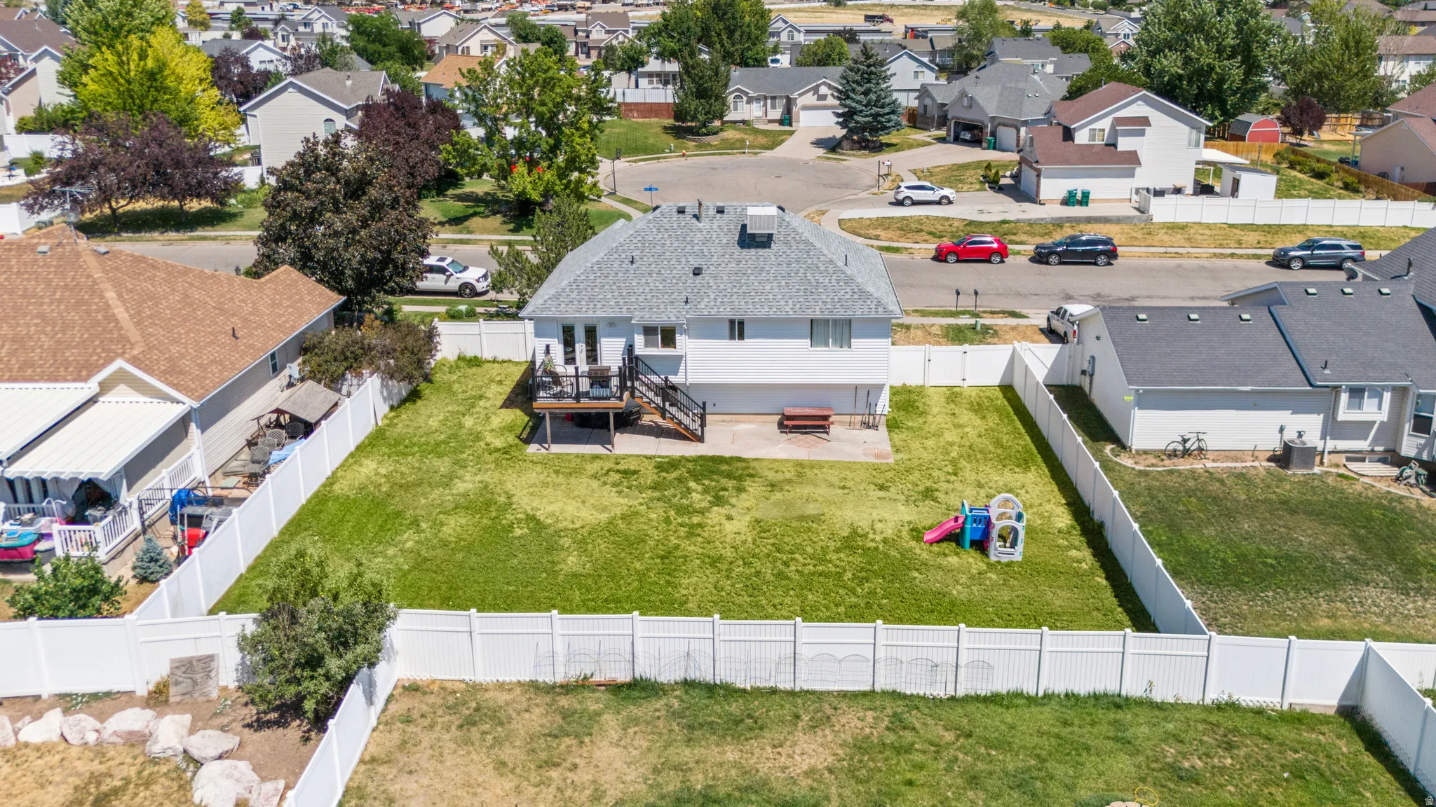 Expansive fenced backyard with a manicured lawn, an elevated deck, and a lower patio area