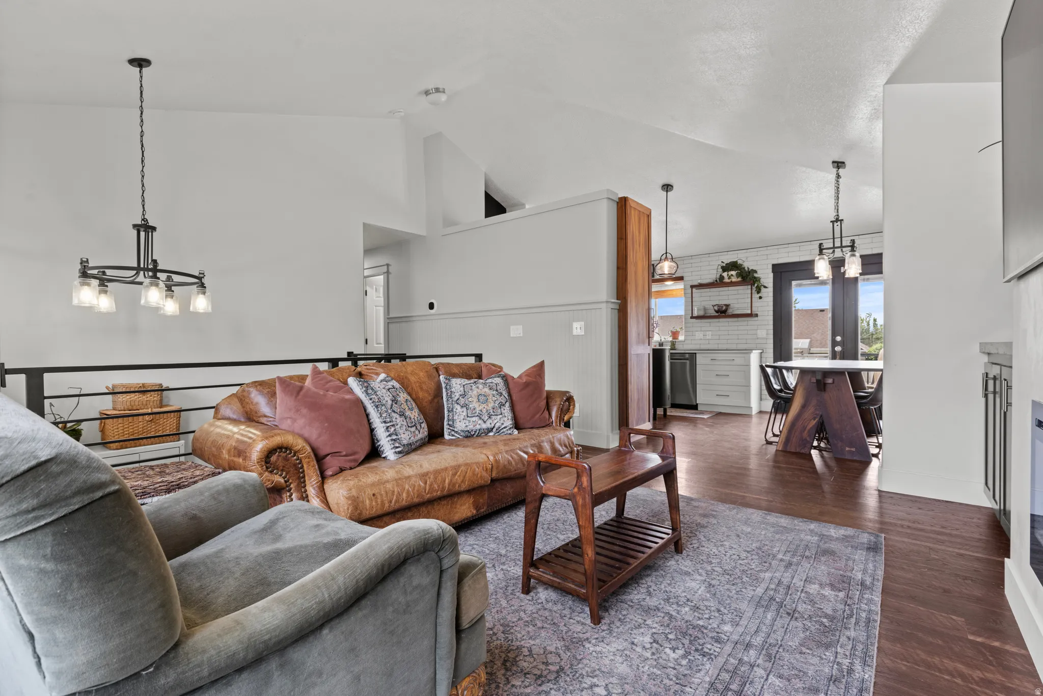 Open-concept living area featuring vaulted ceilings, dark wood-finish flooring, and a modern black metal railing