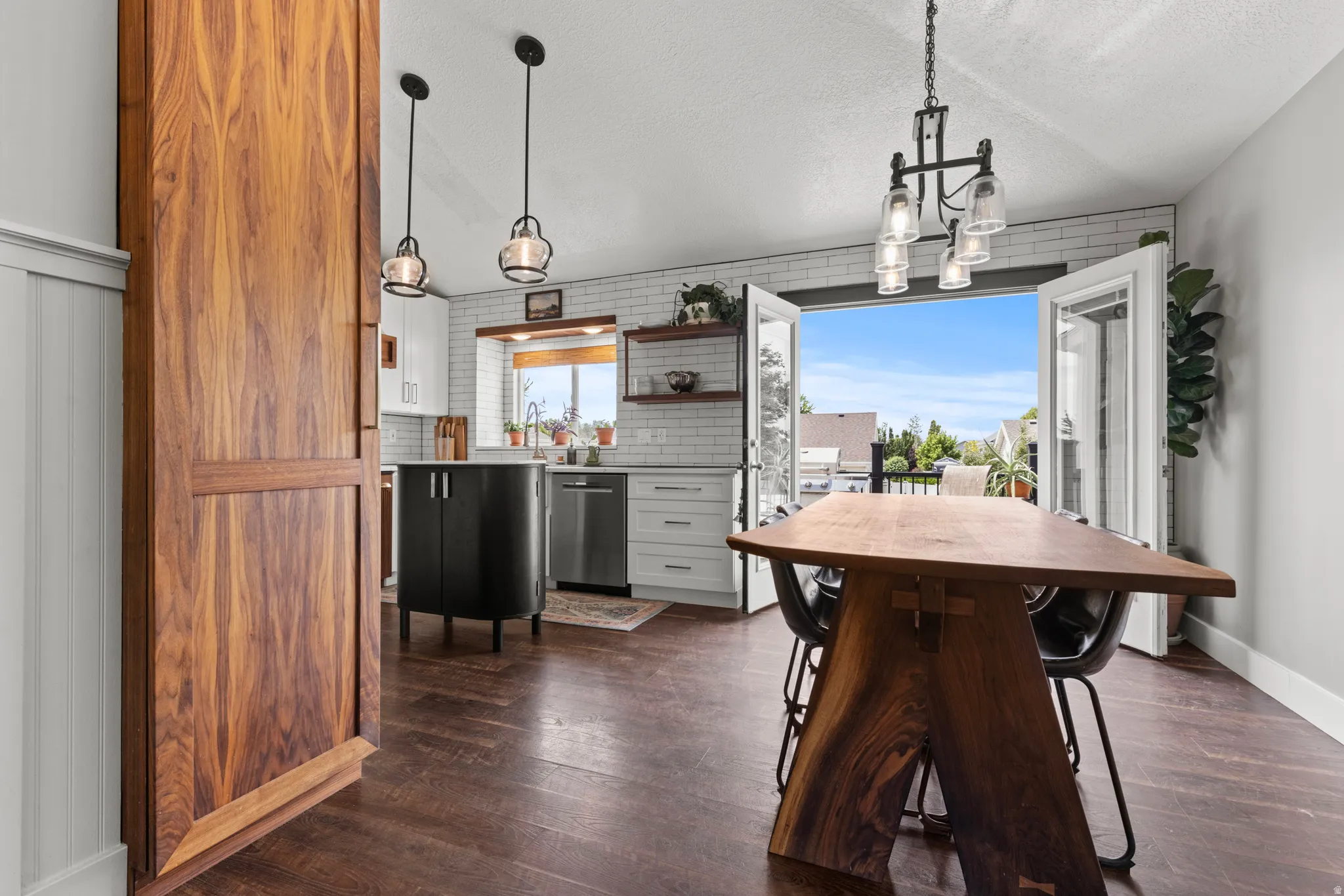 Open-concept dining and kitchen area featuring wood-finish flooring, a wood barn door, and a kitchen with white subway tile backsplash and stainless steel appliances