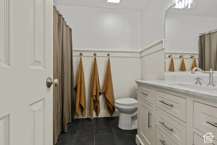 Bathroom featuring a single vanity with a marble-look countertop, white cabinetry with brushed nickel hardware, and dark tile flooring