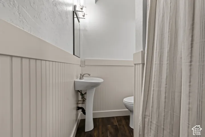 Pedestal sink with brushed nickel faucet, beadboard wainscoting, and wood-finish flooring