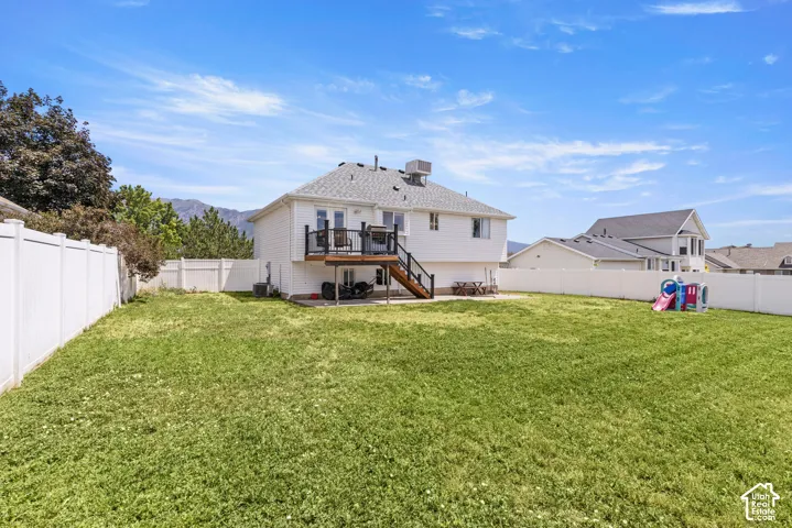Expansive grassy backyard featuring a white vinyl privacy fence, a multi-level deck with dark railing, and a walk-out lower level