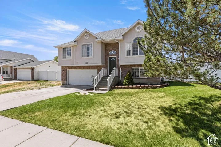 Front exterior featuring a two-car garage, brick facade, arched window, and mature landscaping