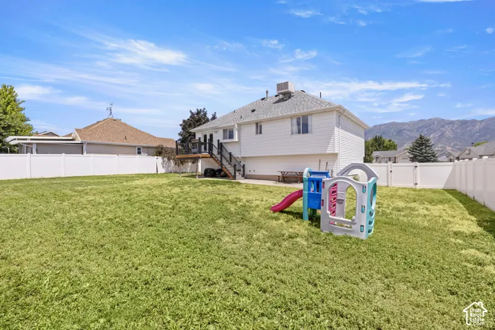 Spacious backyard featuring a manicured lawn, white vinyl fencing, and a multi-level deck with stairs