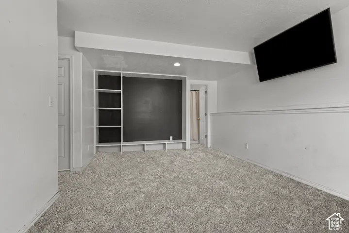 Carpeted room featuring a built-in shelving unit with a dark back panel and a mounted flat-screen display. *Carpet is photoshopped in, ment to match new carpet.