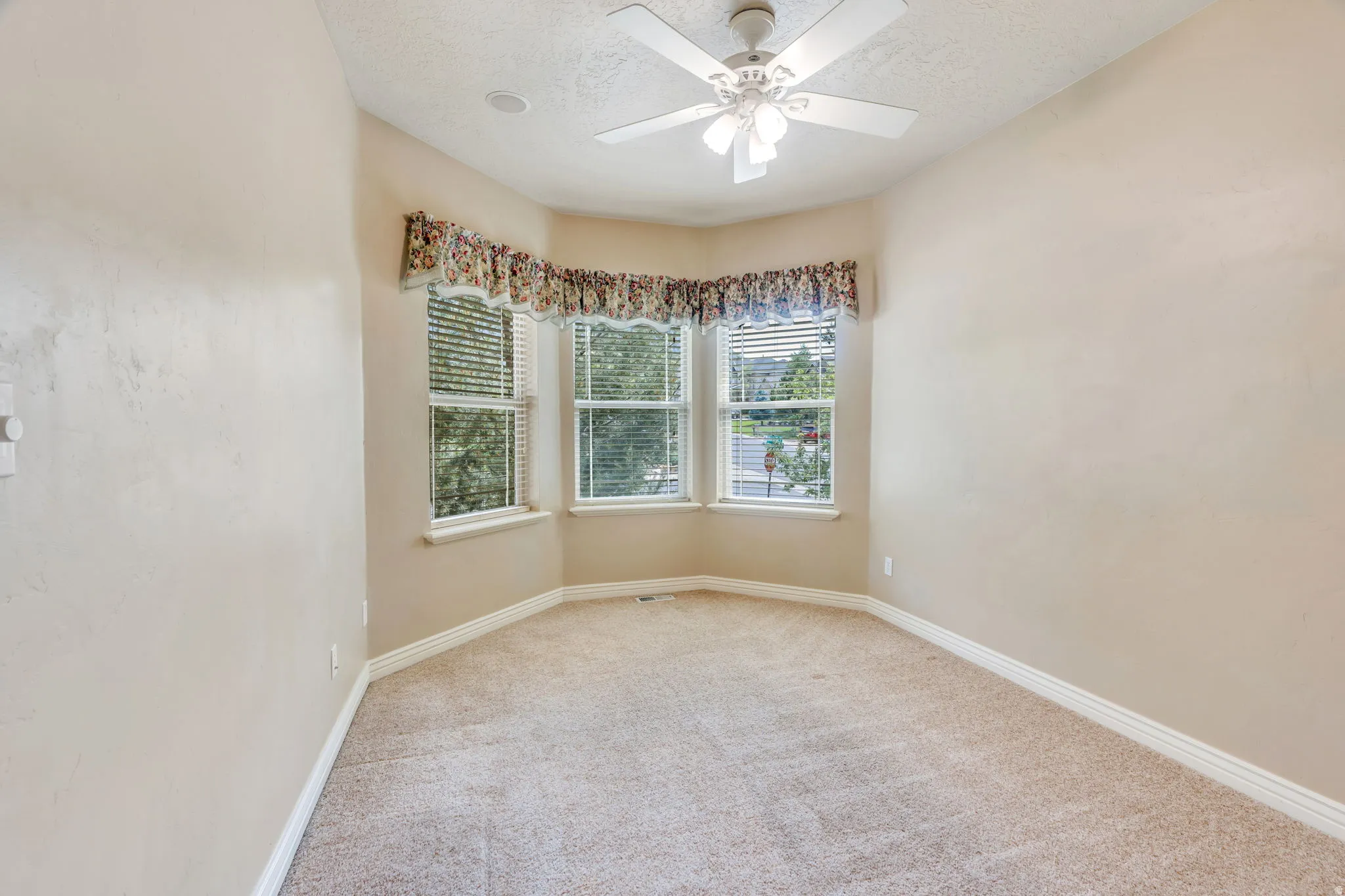 Bay window with blinds, ceiling fan, neutral carpet, and light-colored walls