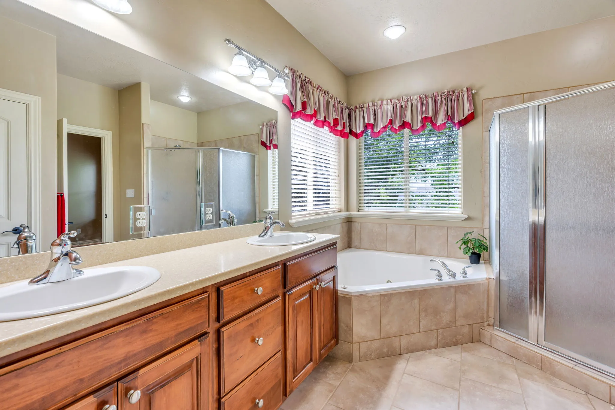 Dual vanity with undermount sinks, a built-in corner soaking tub, a separate glass-enclosed shower, and tile flooring