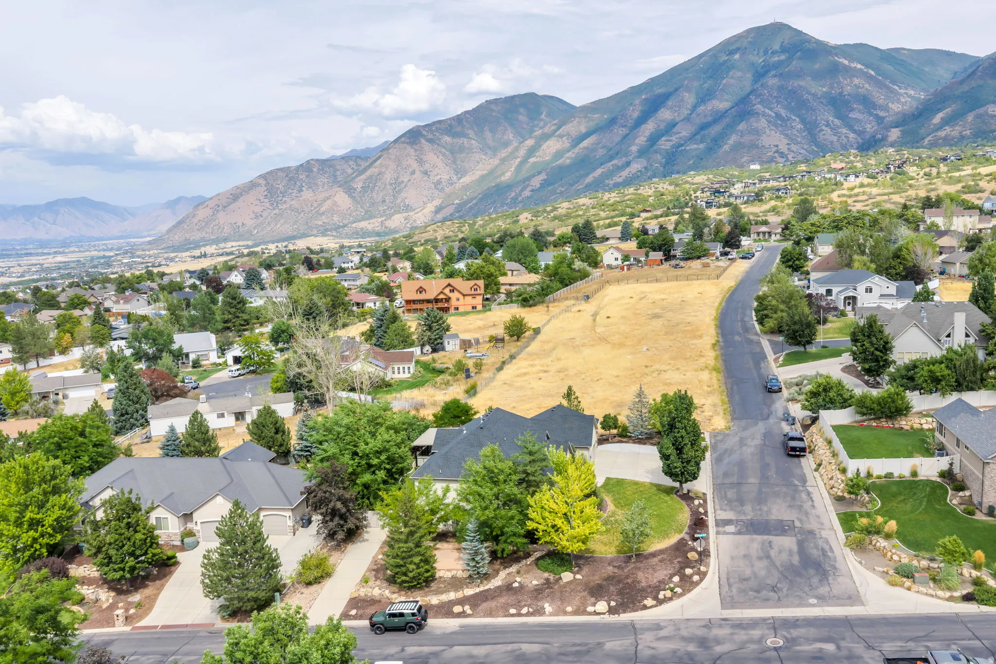Expansive land parcel featuring a gentle slope, surrounded by established residential areas and mature trees, with mountain scenery in the background