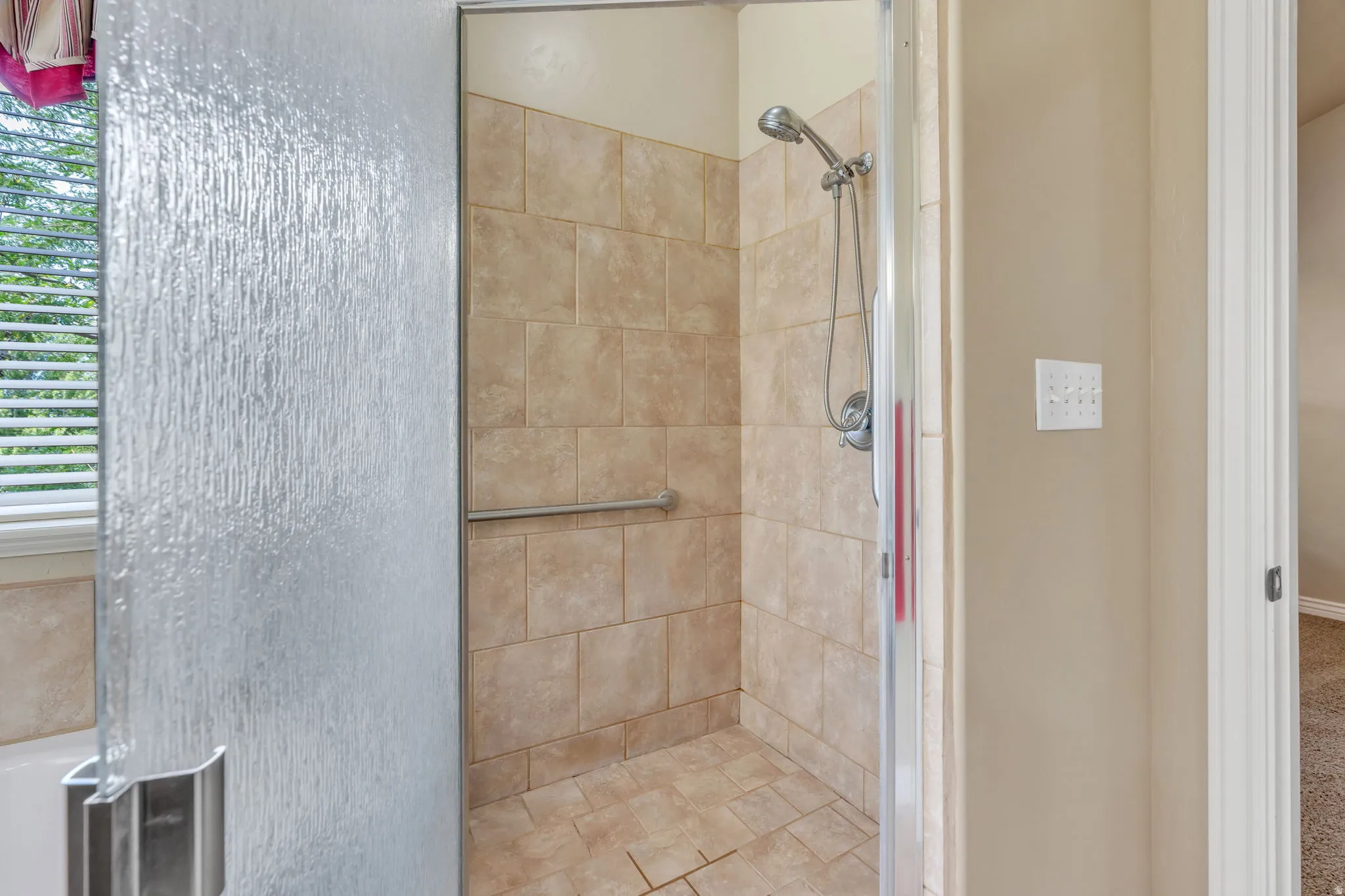 Walk-in shower with full-height tile surround, integrated grab bar, and hand-held shower fixture