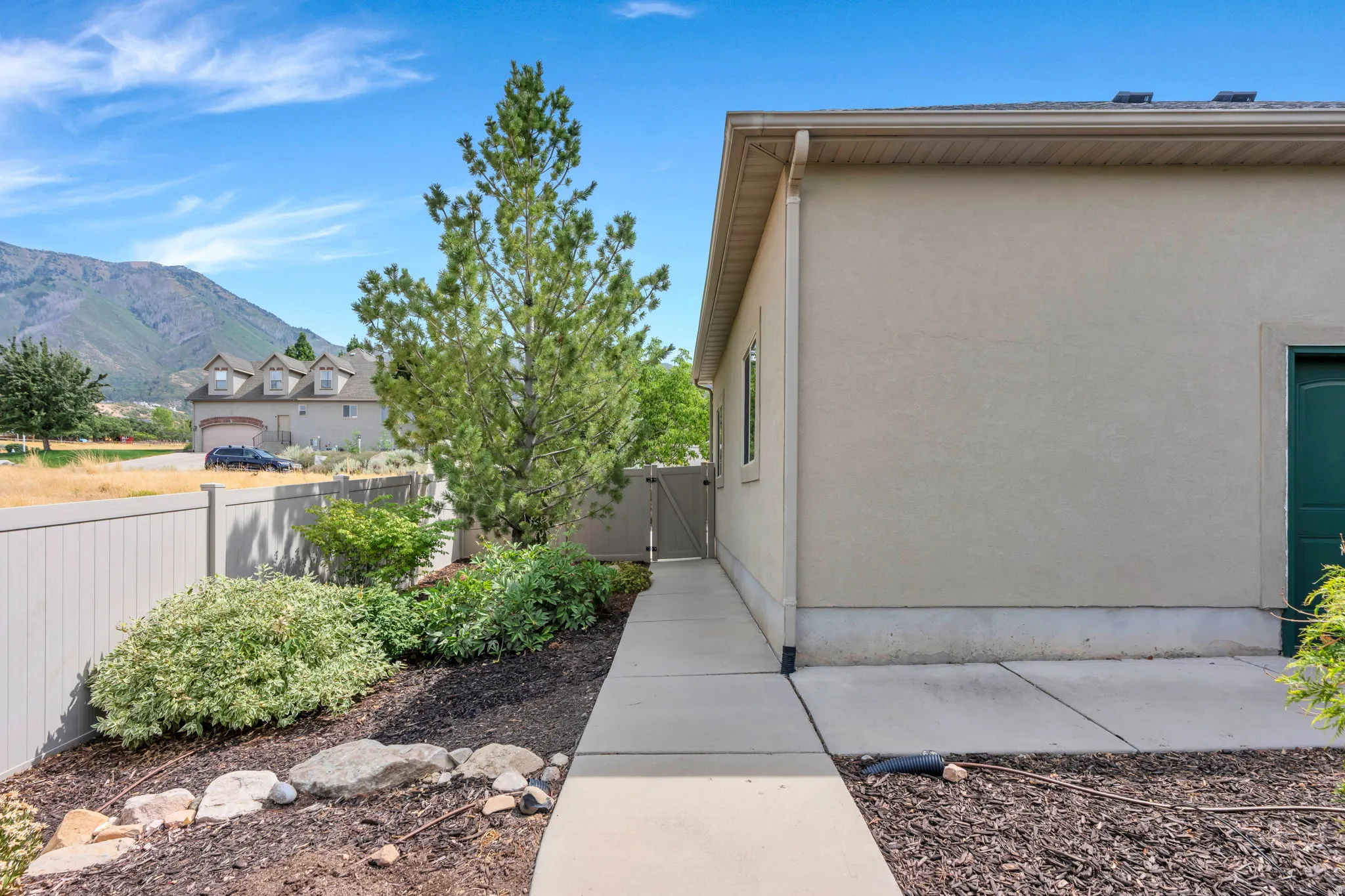 Stucco exterior with a side walkway leading to a gate, mature trees, and established landscaping