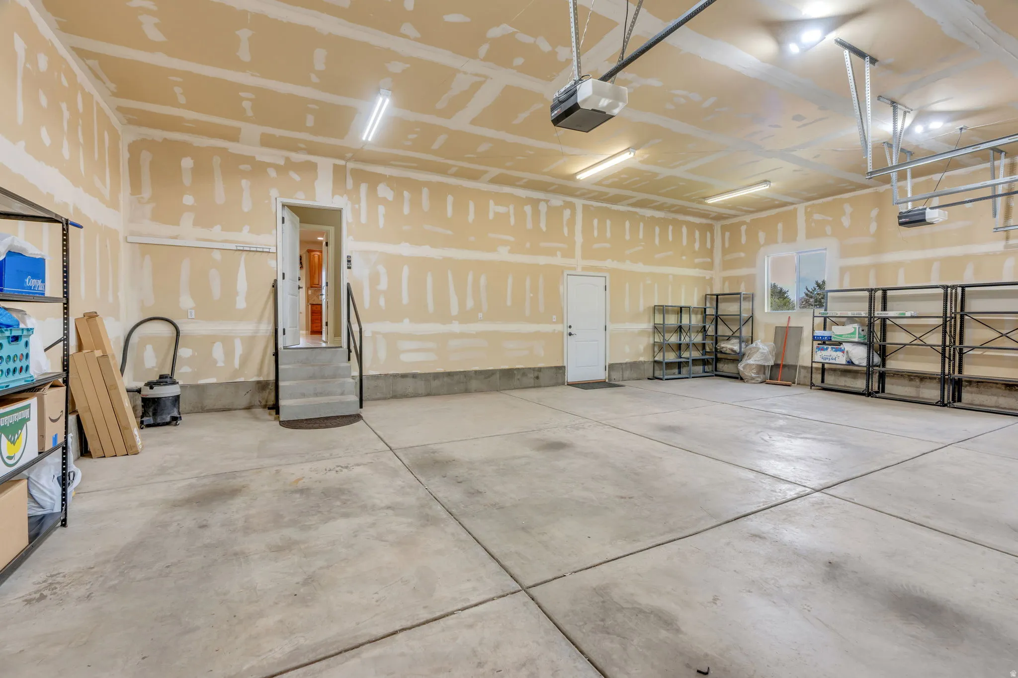 Spacious garage with concrete flooring, multiple overhead lighting fixtures, and direct interior access