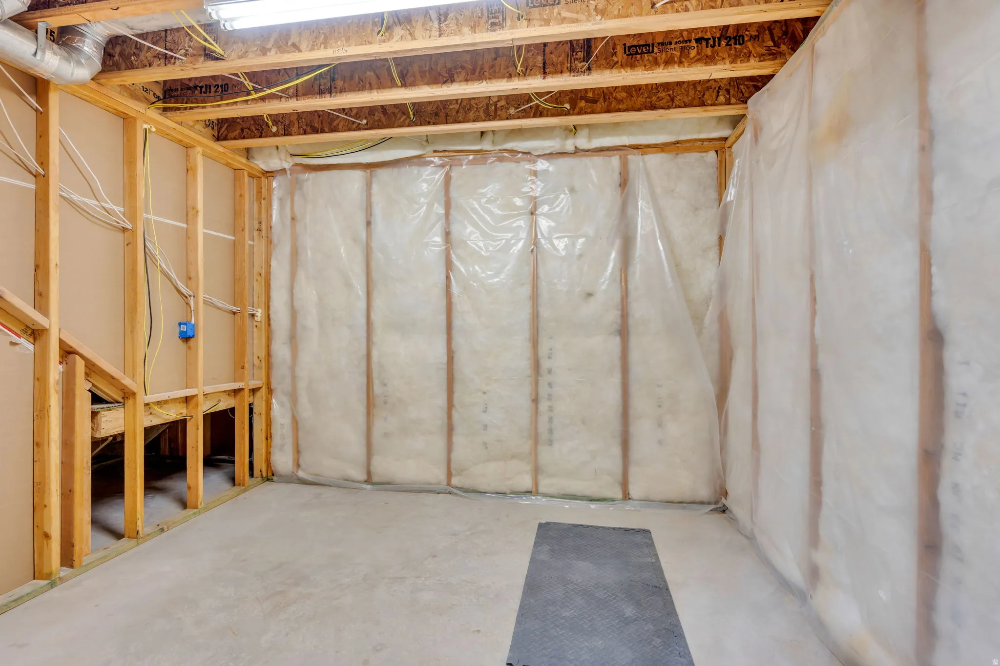 Unfinished basement with exposed wood framing, concrete flooring, and insulated walls