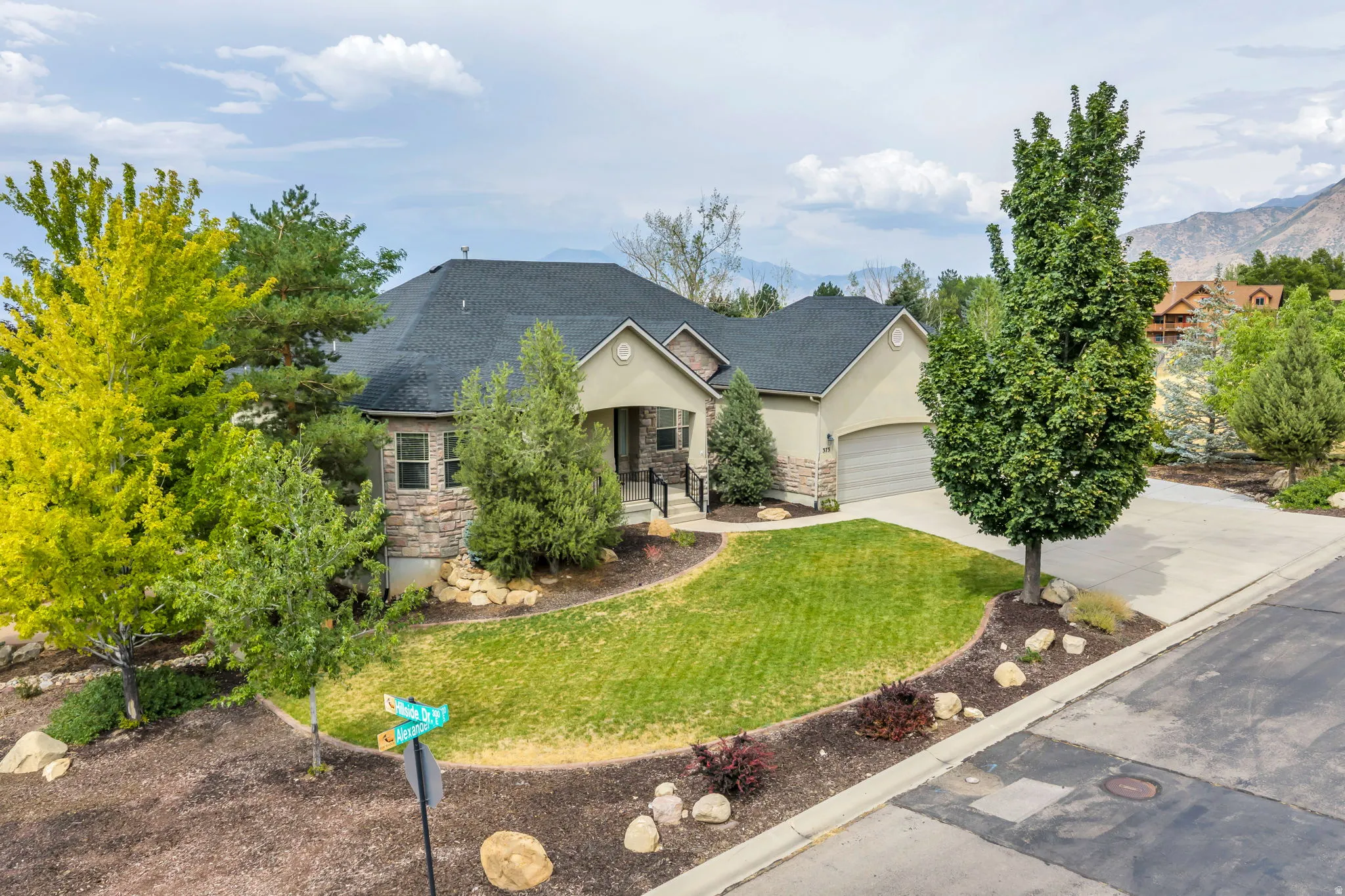 Siding exterior with stone accents, a dark shingle roof, a concrete driveway, and a manicured lawn