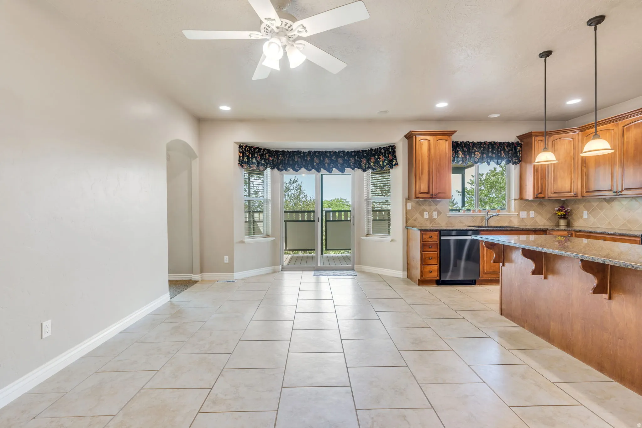Tile flooring, wood cabinetry, granite countertops, built-in dishwasher, and a ceiling fan with integrated lighting