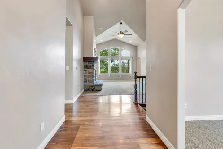 Vaulted ceiling with a ceiling fan, stone fireplace with a wood mantel, large arched windows, wood-finish flooring, and a wrought iron railing