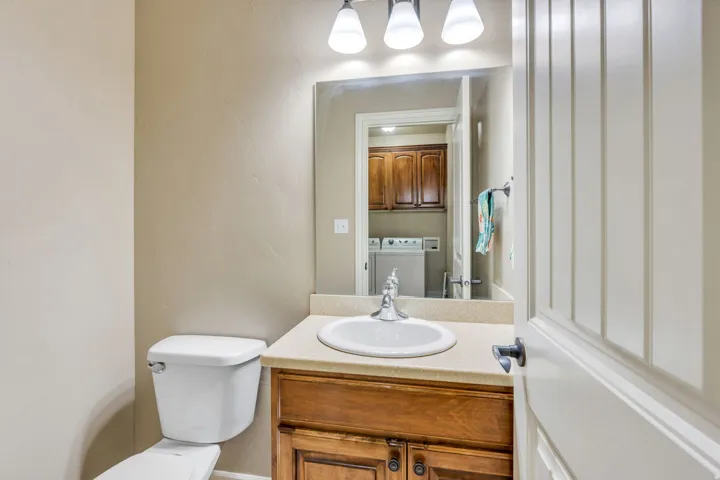 White toilet, wood-finish vanity with built-in sink, and a vanity mirror with overhead lighting