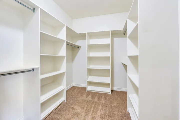 Walk-in closet featuring built-in shelving, multiple hanging rods, and carpet flooring