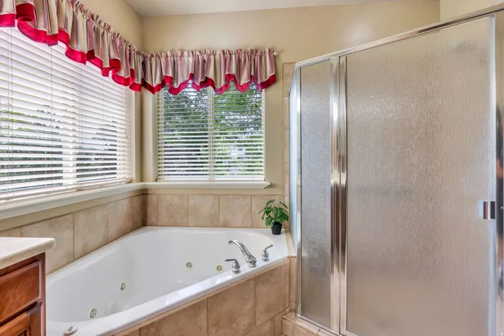 Jetted soaking tub with tile surround, framed by two windows with horizontal blinds