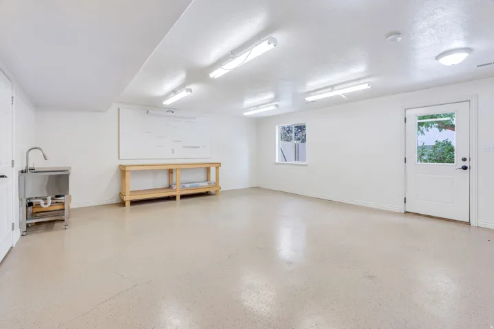 Spacious utility room featuring a built-in utility sink, multiple overhead light fixtures, a large window, and a white exterior door with glass paneling