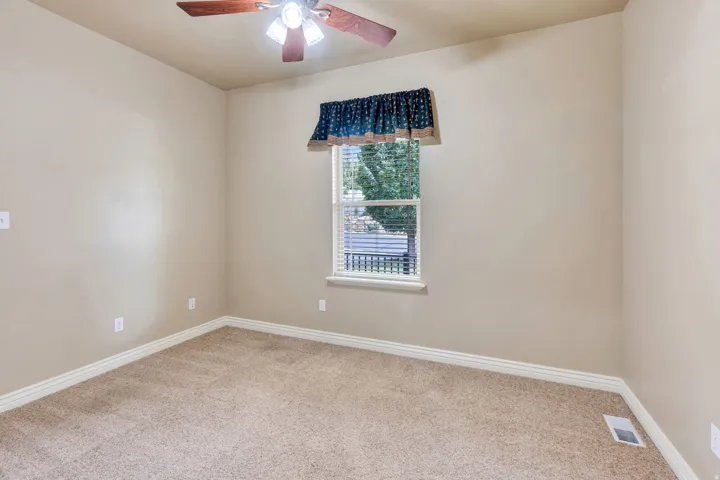 Textured carpeting, neutral wall color, ceiling fan with integrated lighting, window with blinds