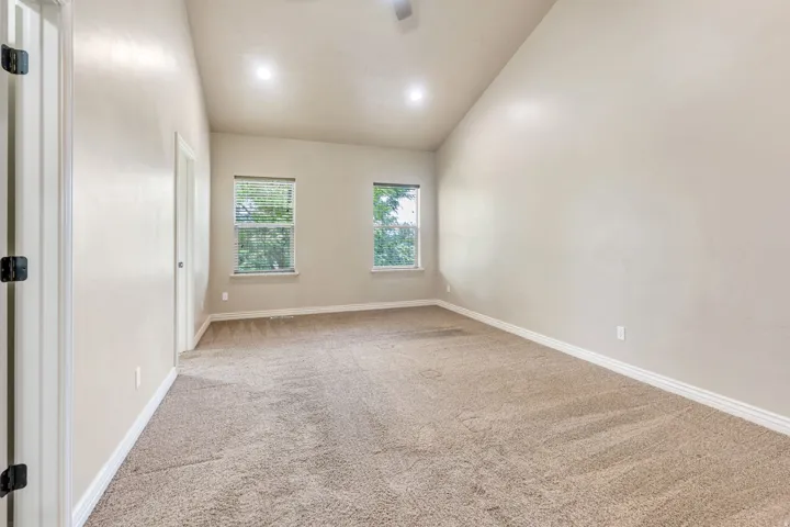 Vaulted ceiling, recessed lighting, two windows with blinds, light-toned carpet, and white trim