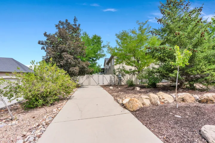 Paved driveway with a metal gate, surrounded by mature trees, shrubs, and natural rock landscaping