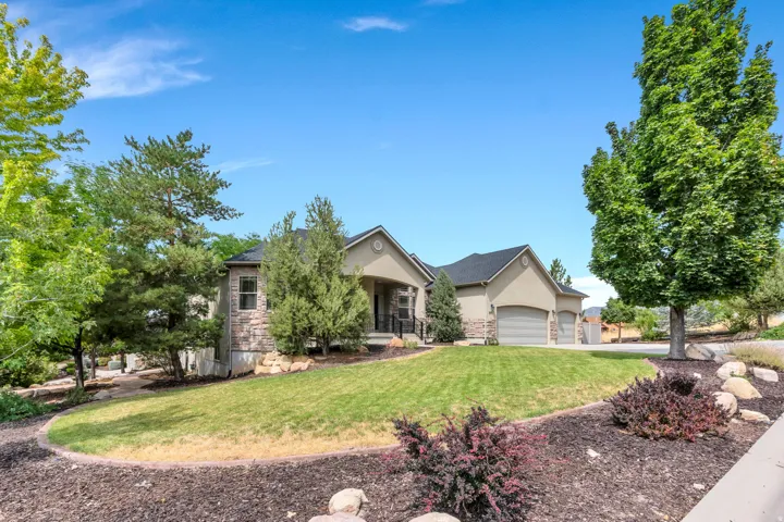 Stucco and stone exterior, covered entry, attached garages, established landscaping, and a sloped lawn