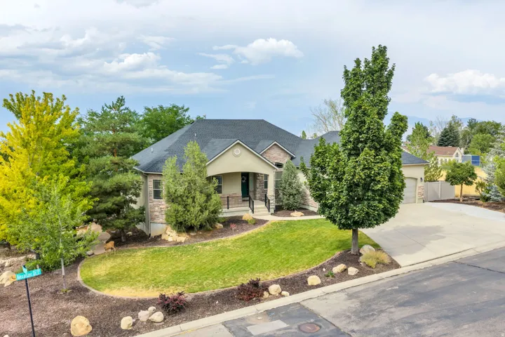 Stucco and stone exterior with a covered porch, attached garage, and mature landscaping
