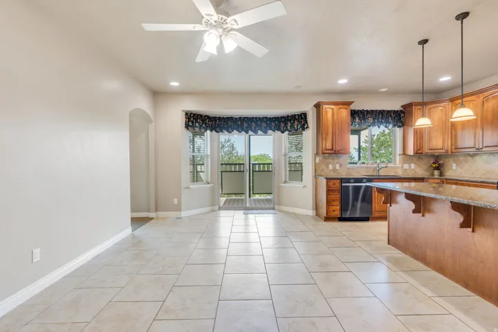 Tile flooring, wood cabinetry, granite countertops, built-in dishwasher, and a ceiling fan with integrated lighting