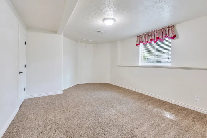 Carpeted room featuring a white door with black hardware, a window with blinds, and a flush mount ceiling light