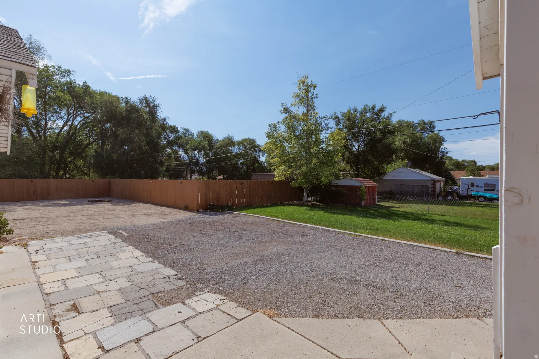 Expansive backyard area featuring a gravel surface, a wooden privacy fence, natural grass sections, and mature trees