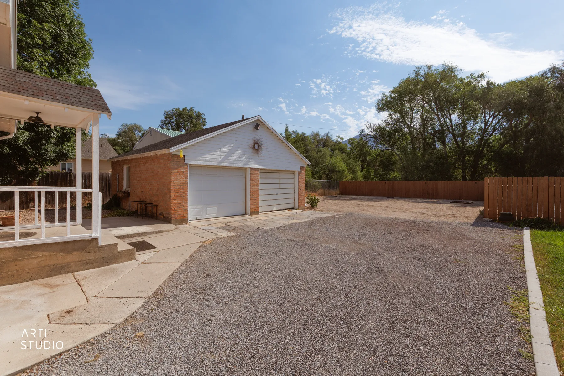 Two-car garage with brick siding, white garage doors, and an expansive gravel driveway